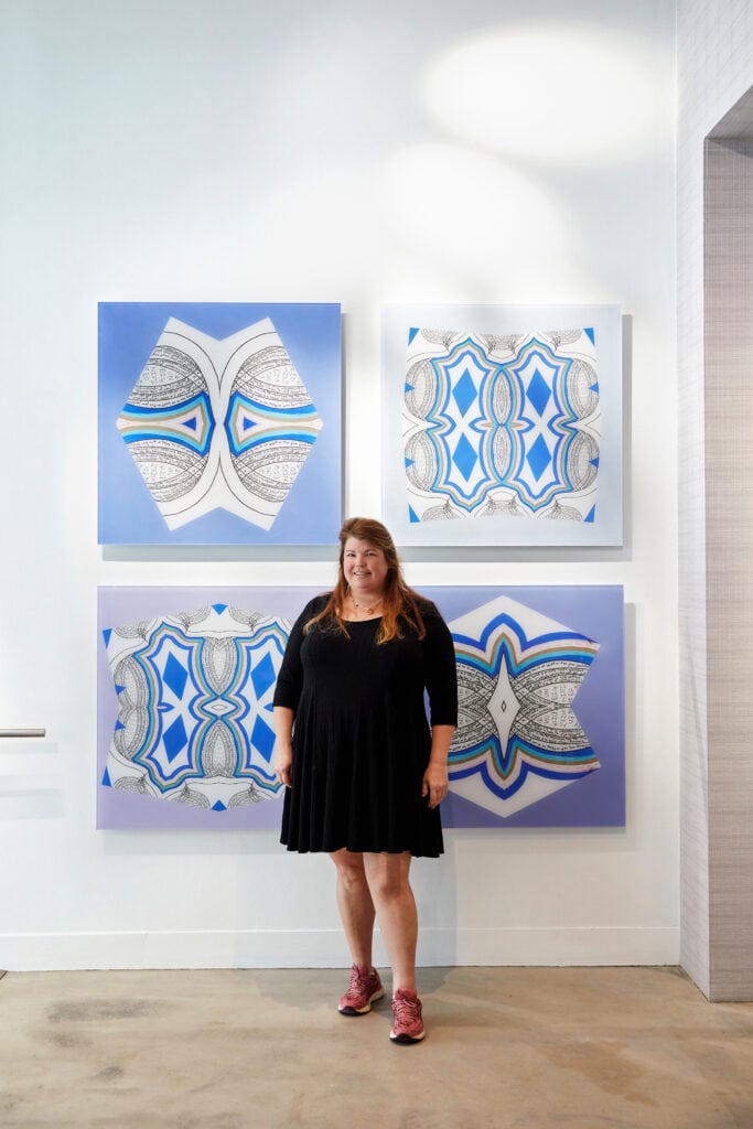 Anna Lou Curnes, Glass Artist, standing in front of her Faith series of wall art