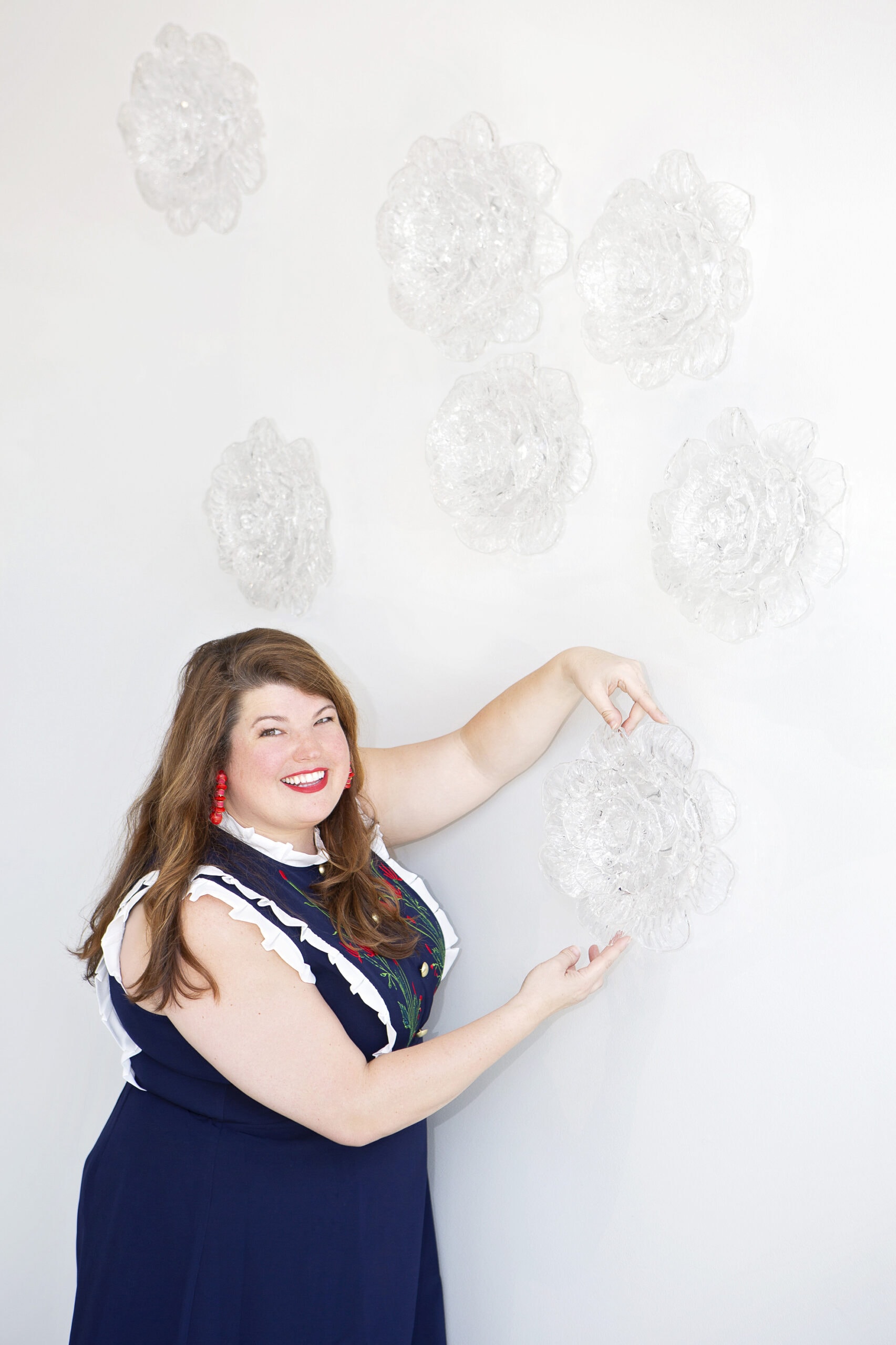 Anna with hot glass flower installation on a white wall