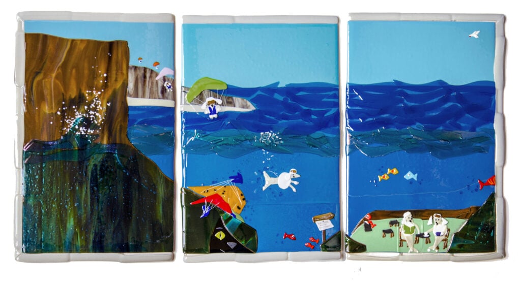 Handmade, original fused glass wall art of the ocean with cliffs on the left, paragliders in the middle and people having a picnic on the right.