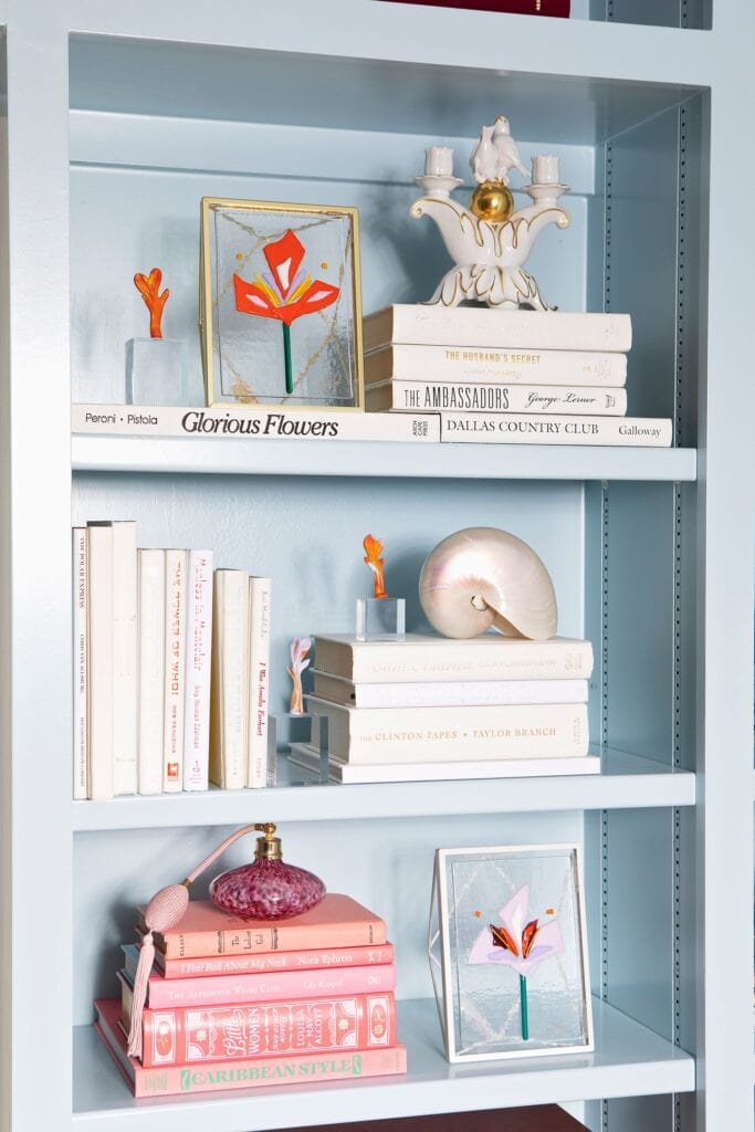 Blue bookshelves containing books, fused glass floral art and ornaments